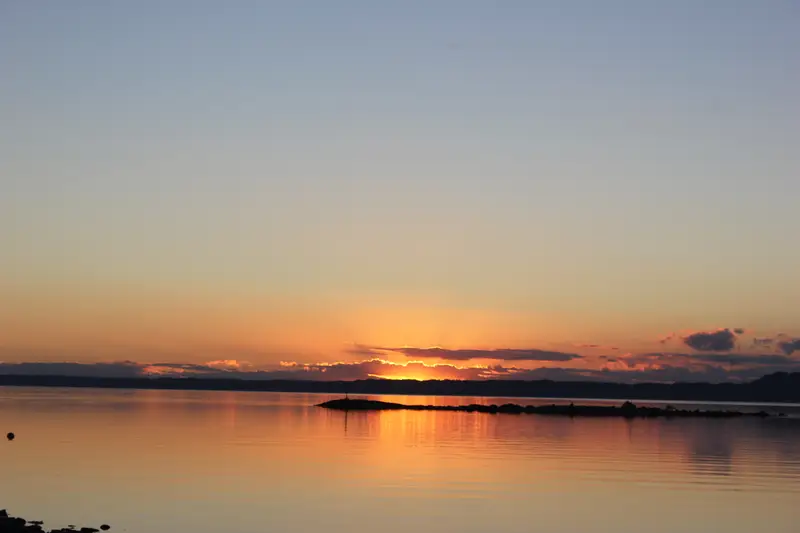 Atardecer naranjo sobre el lago con la orilla en sombra